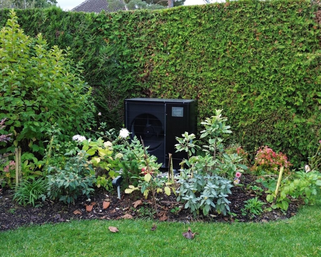 image d'un jardin fleuri à Nyon avec une pompe à chaleur à peinture noir